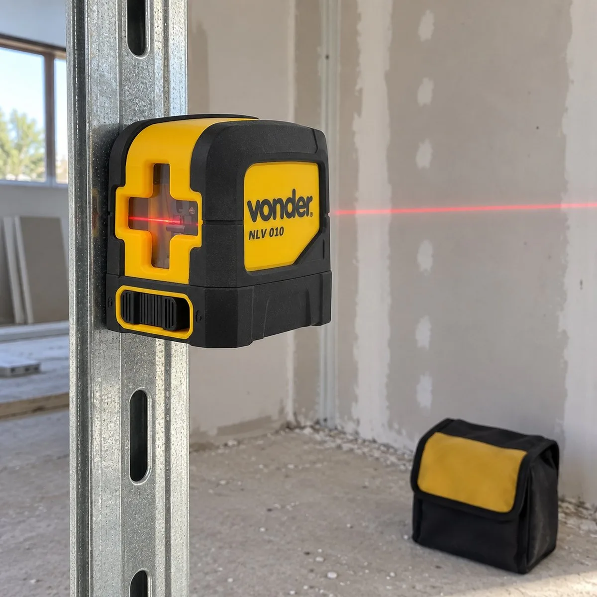 Nível amarelo da Vonder preso pelo ímã num montante de aço, riscando uma linha vermelha na parede de gesso; a bolsa fica no chão